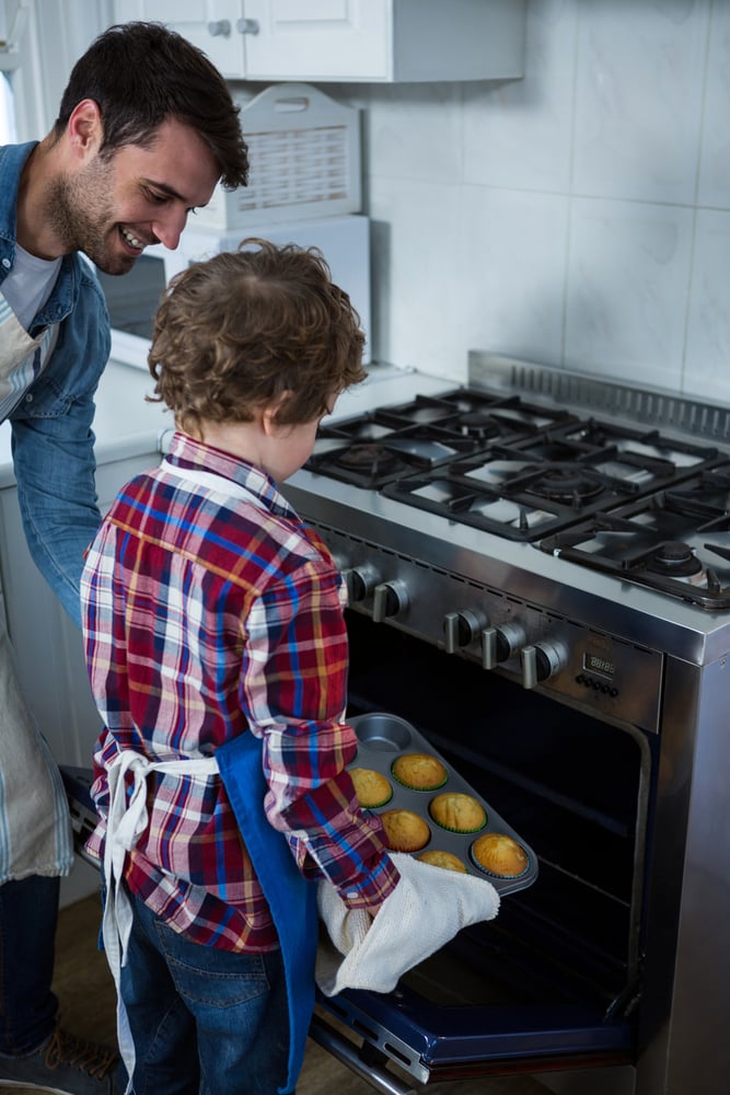 Father and son placing cupcakes tray in oven in the kitchen