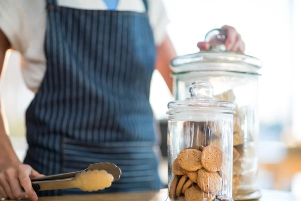 Mid-section of waitress holding jar and tong in cafx92xA9