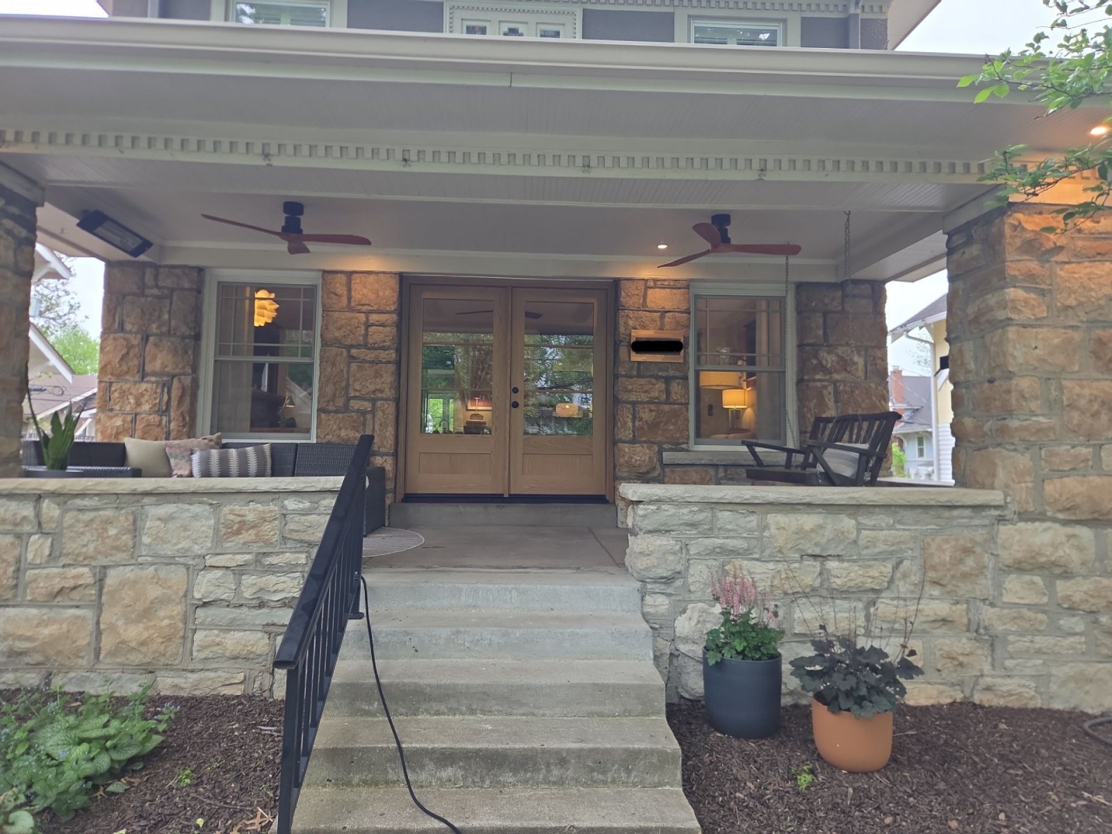 Craftsman-style front porch with new wood-look double entry doors flanked by stone columns, part of a home renovation project in Kansas City, MO