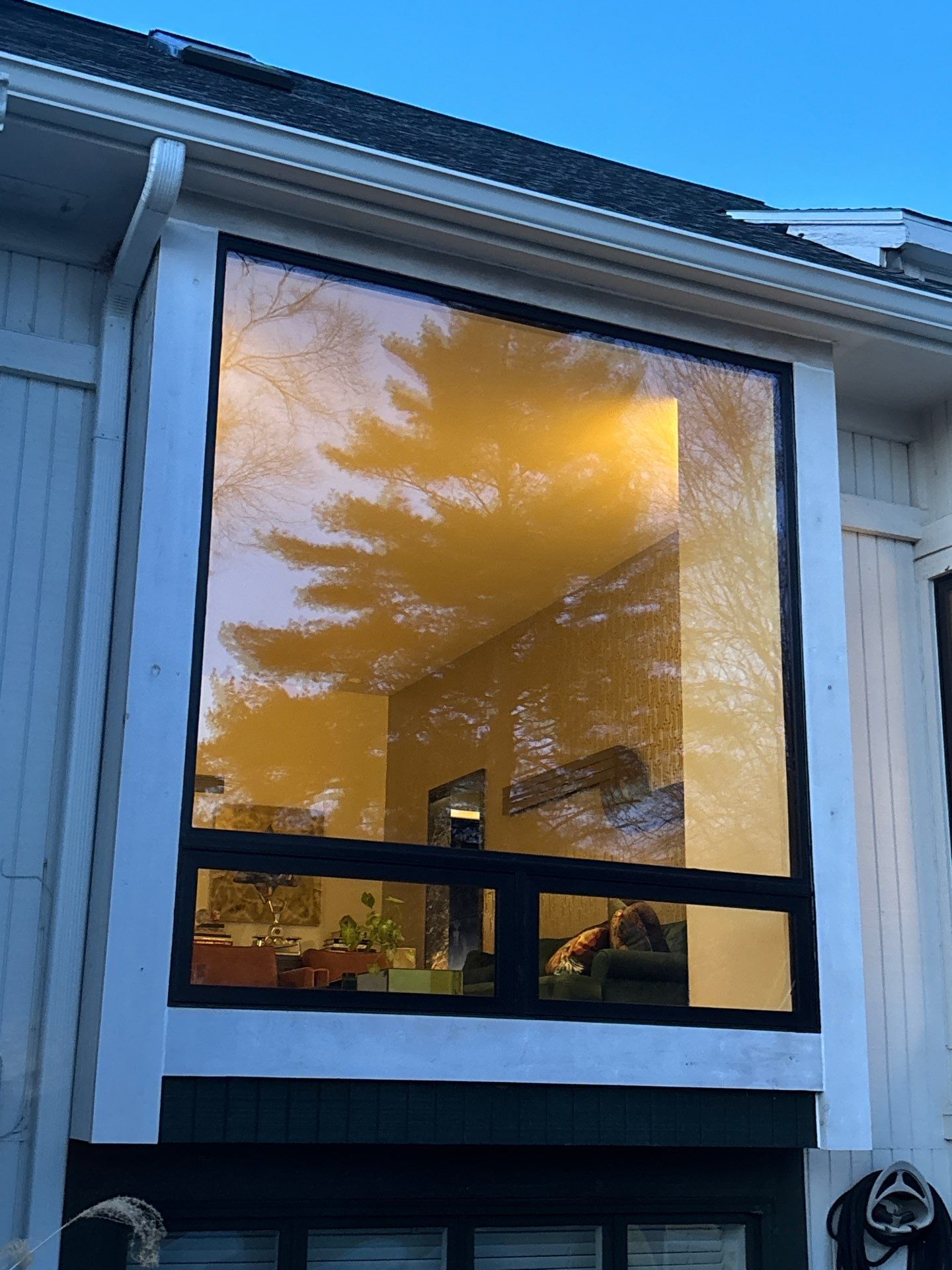 Large black-framed picture window with sliders reflecting trees at sunset on a two-story home in Overland Park, KS