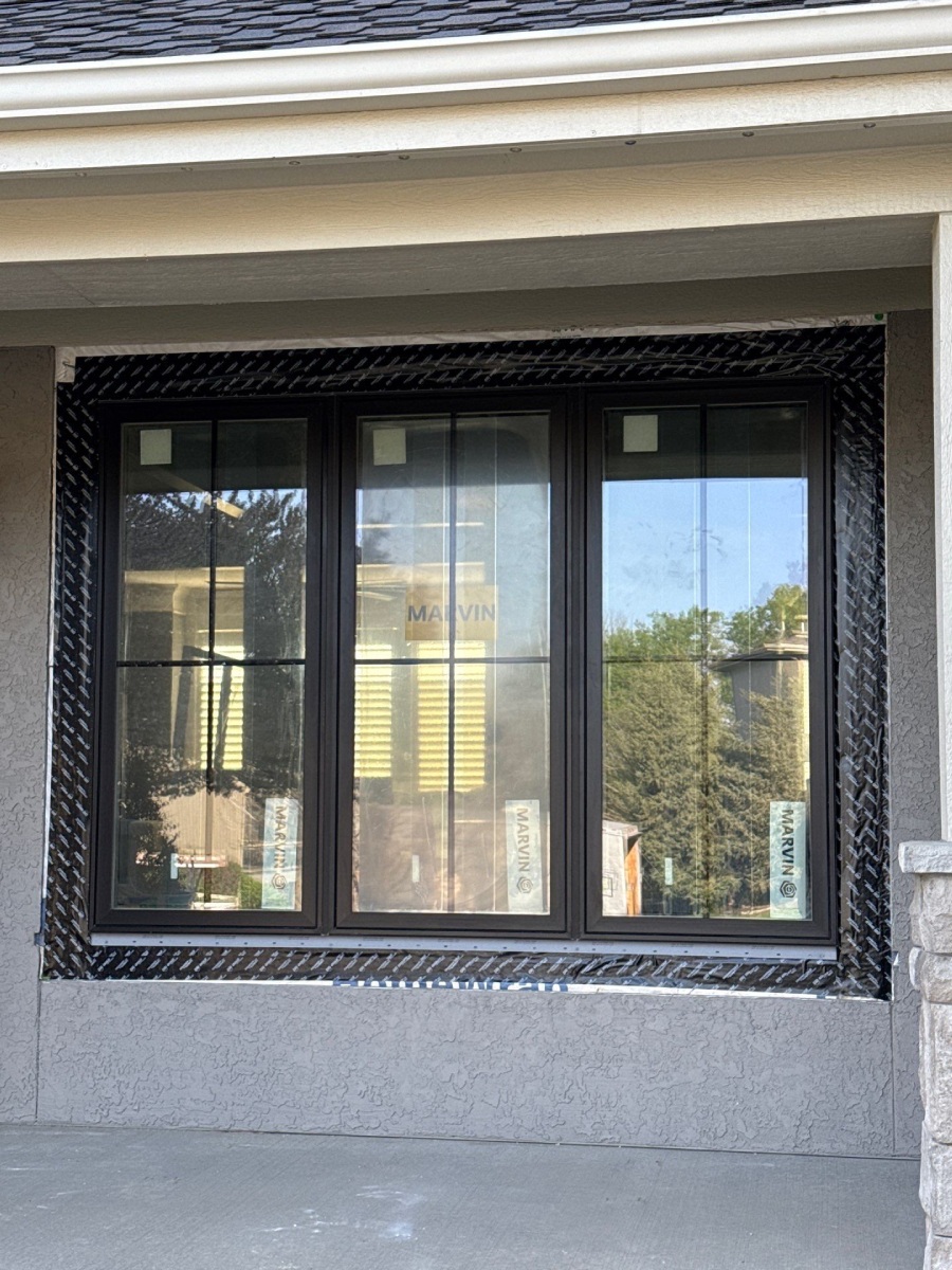 Newly installed black-framed Marvin three-panel window with house wrap tape on a stucco home in Lenexa, KS