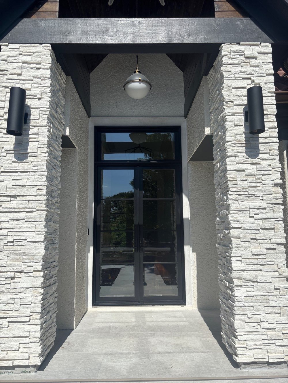 Black-framed double entry doors with transom window, framed by stacked stone columns on a modern home in Lenexa, KS