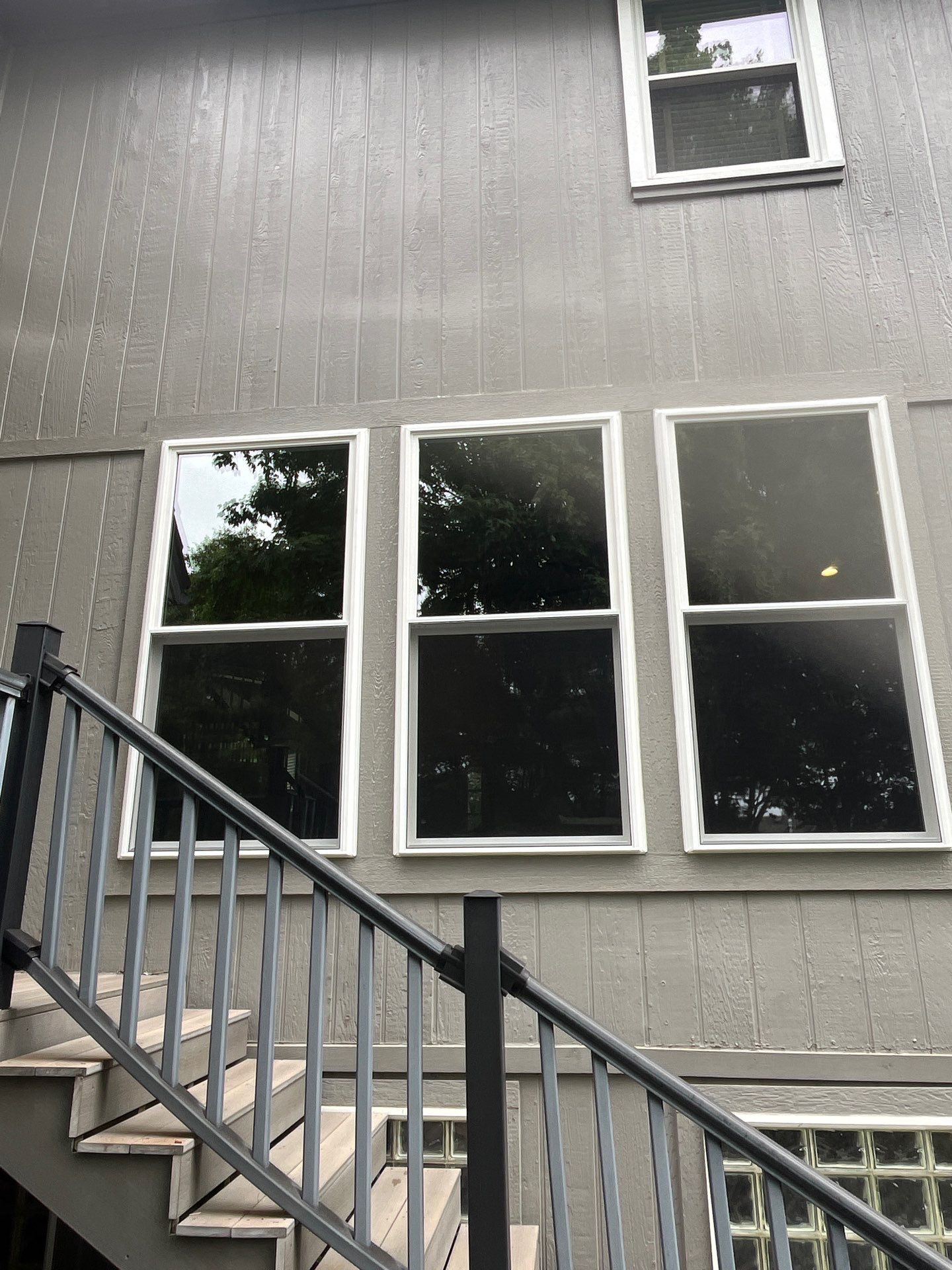 Three new white double-hung windows on gray siding above a deck staircase, exterior of an Olathe, KS home