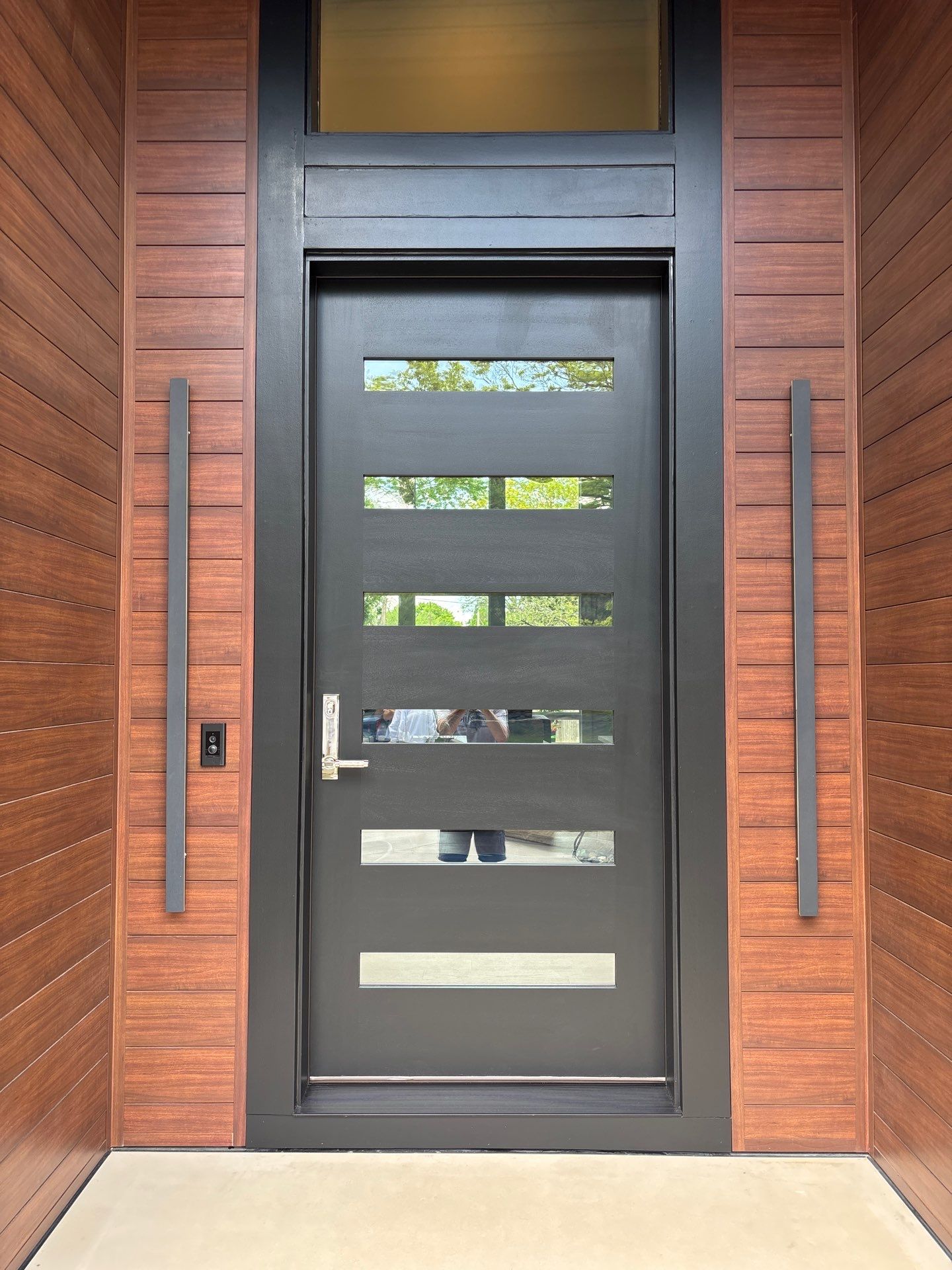 Modern black front entry door with horizontal glass panels on a wood-paneled home in Prairie Village, KS