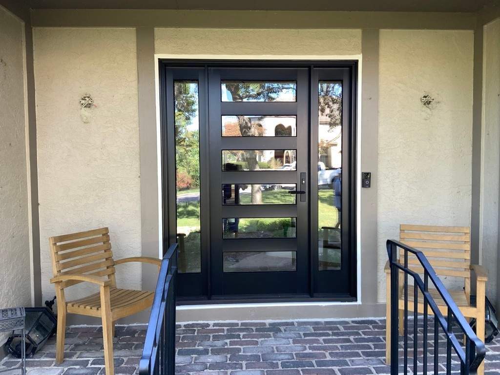 Black front door with five horizontal glass panels and two sidelites, set in a stucco entry with teak chairs on the porch.