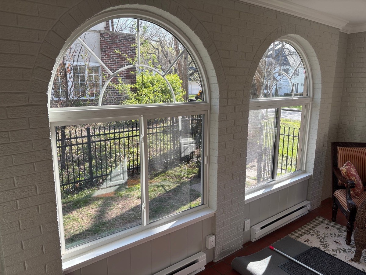 Interior view of white-framed arch top windows in a sunroom overlooking a wrought iron fence and neighboring house